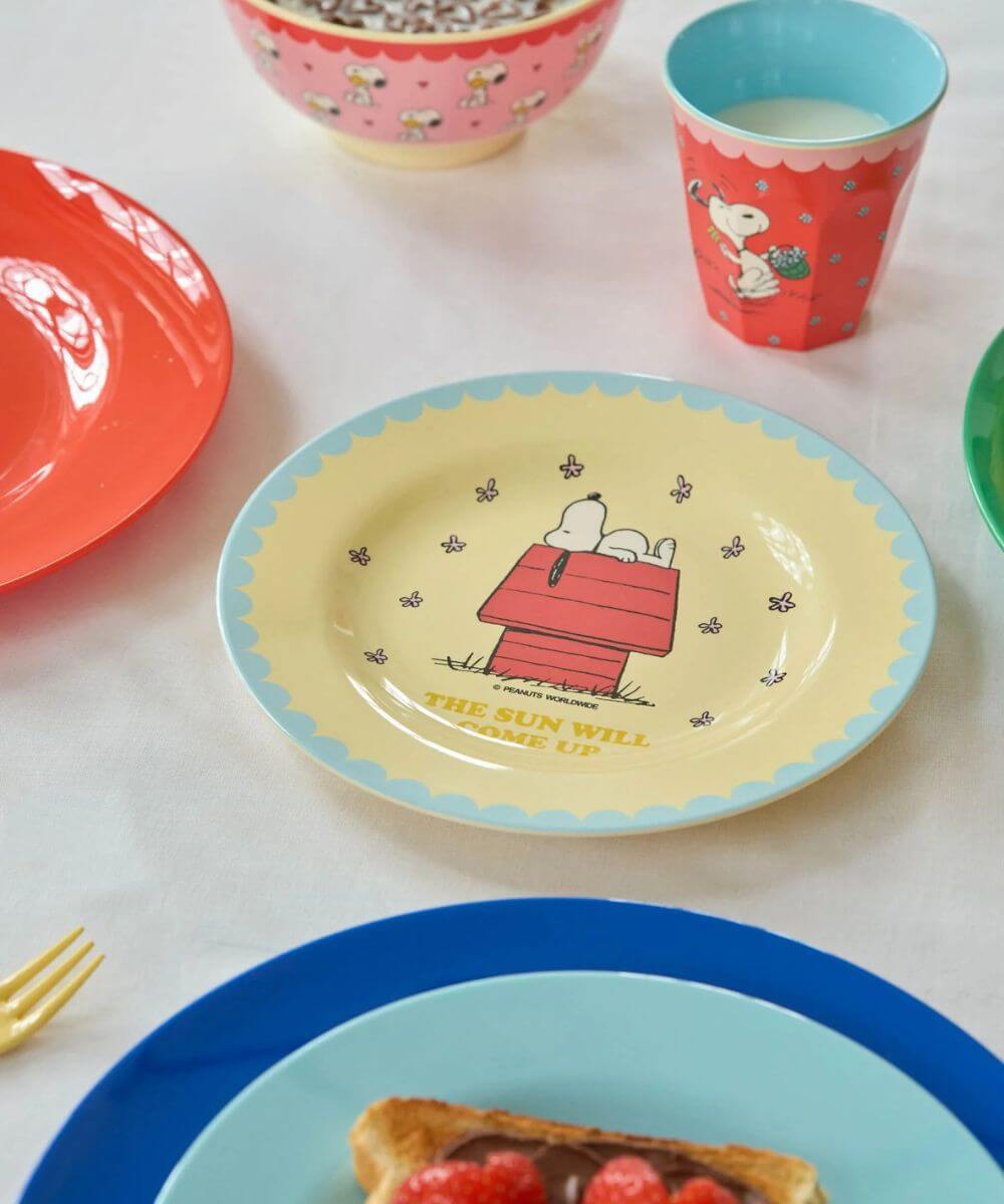 Assiette creuse en mélamine de la collaboration Snoopy écru de la marque Rice, posé sur une table avec le gobelet rouge snoopy