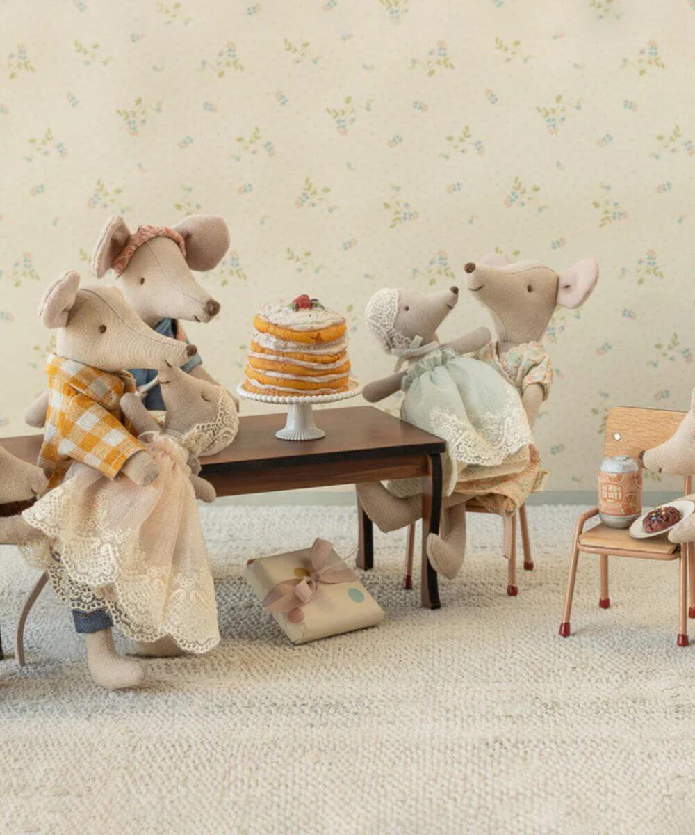 Scènette représentant une famille de souris Maileg à table, certaines portant dans les bras le bébé souris en robe poudre dans les bras