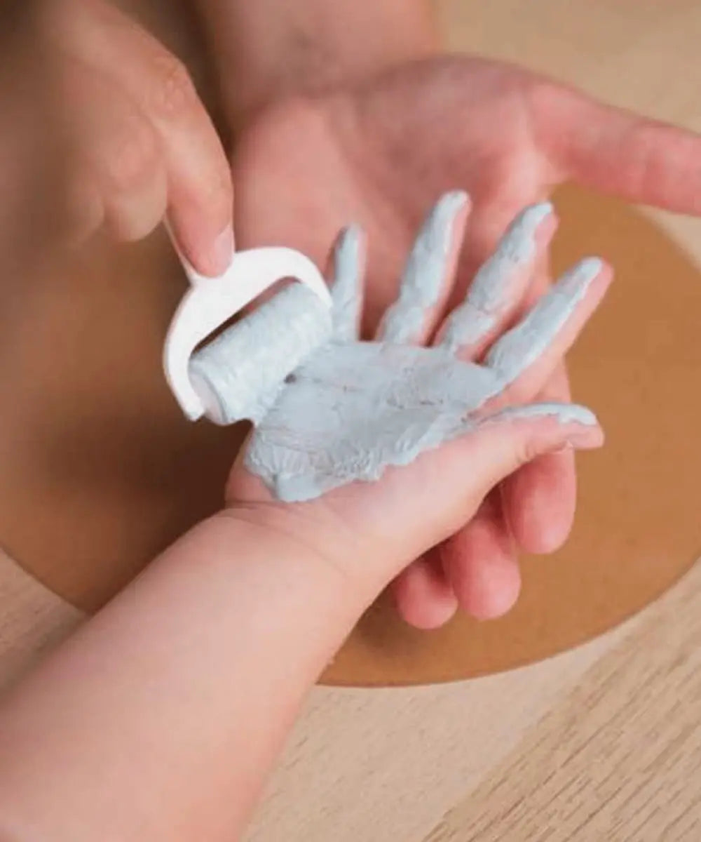 Papa en train de peindre la main d'un bébé pour réalisé le Cadre Empreintes Famille de Petit Artichaut