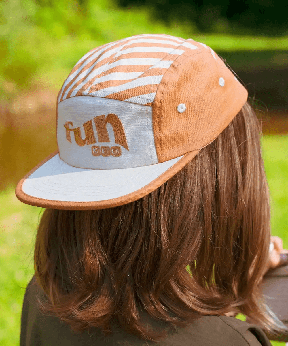 Casquette rayée sable dorée Ki ET LA portée par une fille vue de dos, fond nature verdoyant