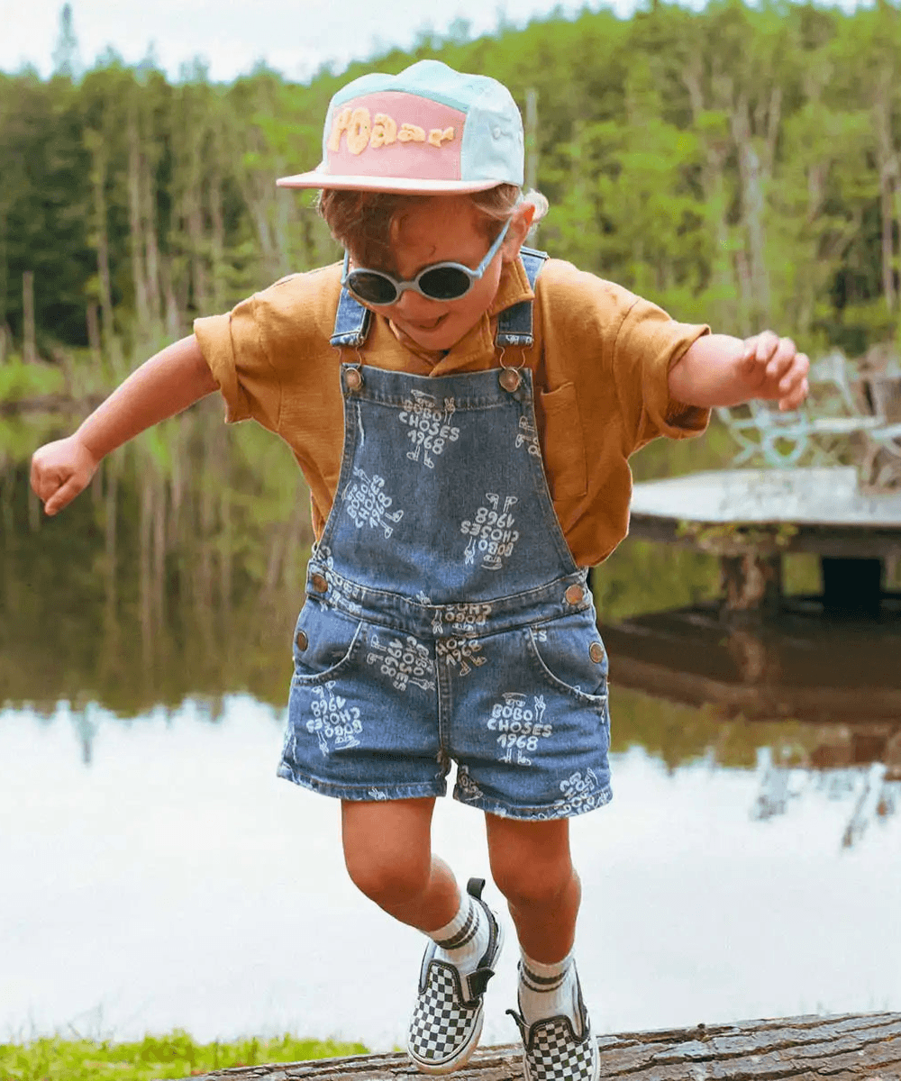 Enfant en mouvement portant la casquette Roar de la marque Ki ET LA, au bord d'un étang