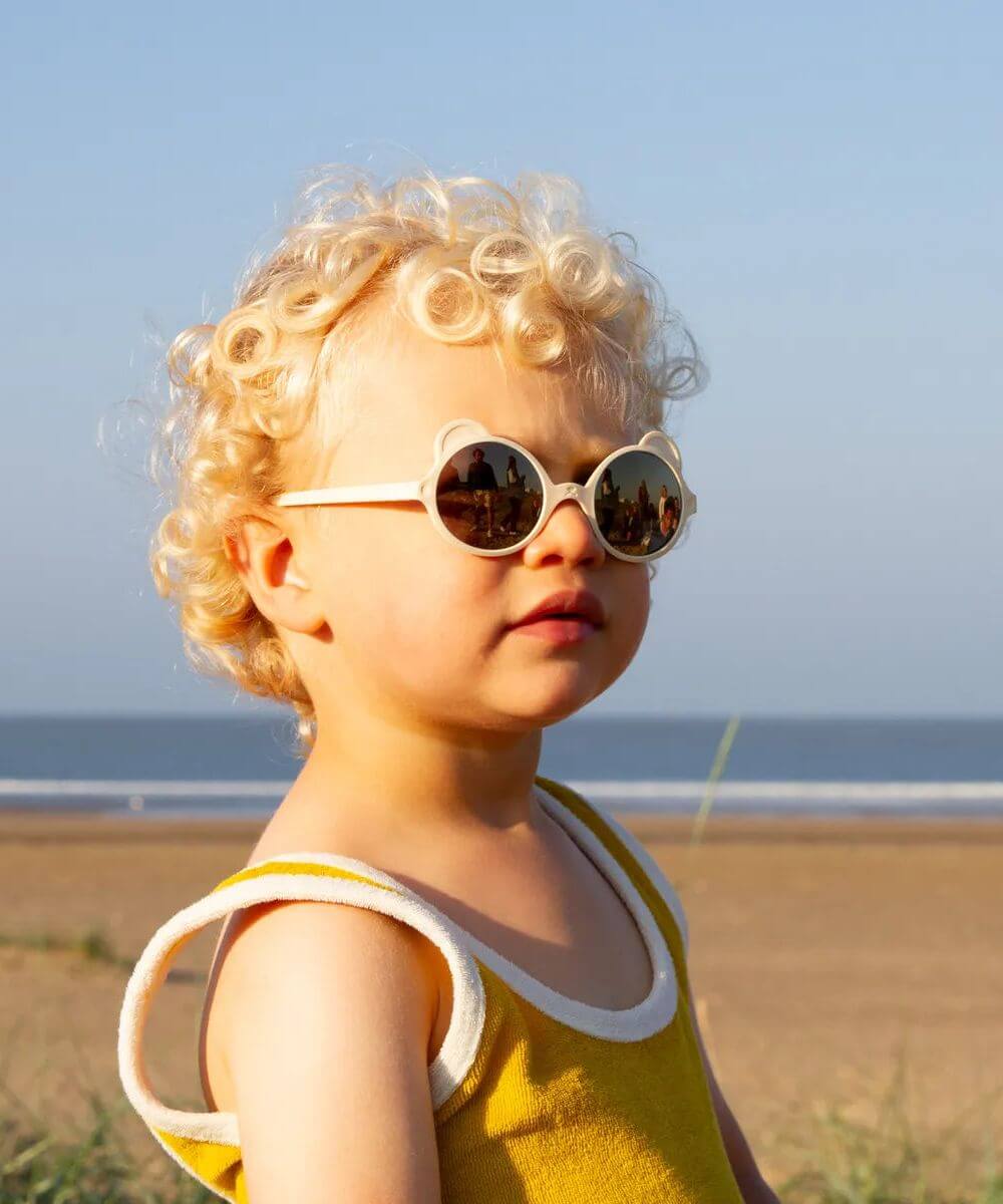 Lunettes Ourson Crème de la marque KI ET LA, portées par un enfant sur la plage
