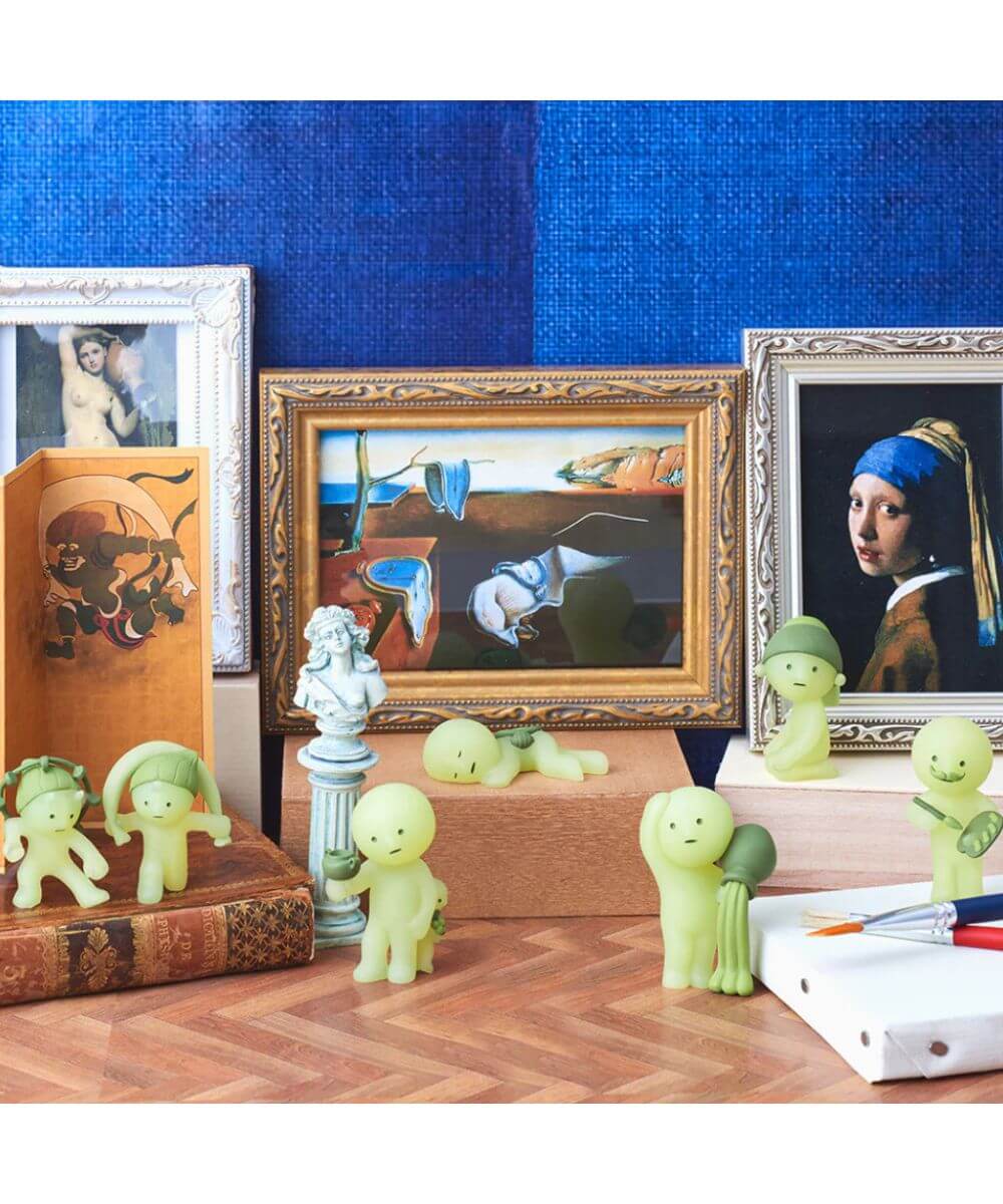 Vue des 6 figurines SMISKI Museum sur une table avec des tableaux en fond