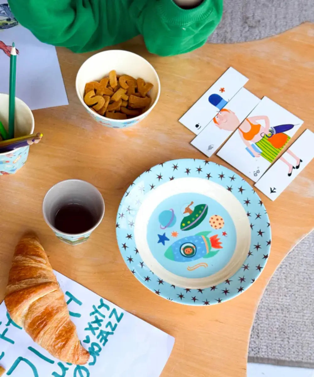 Assiette creuse en mélamine Dogs in Space de la marque danoise Rice posée sur une table d'enfant