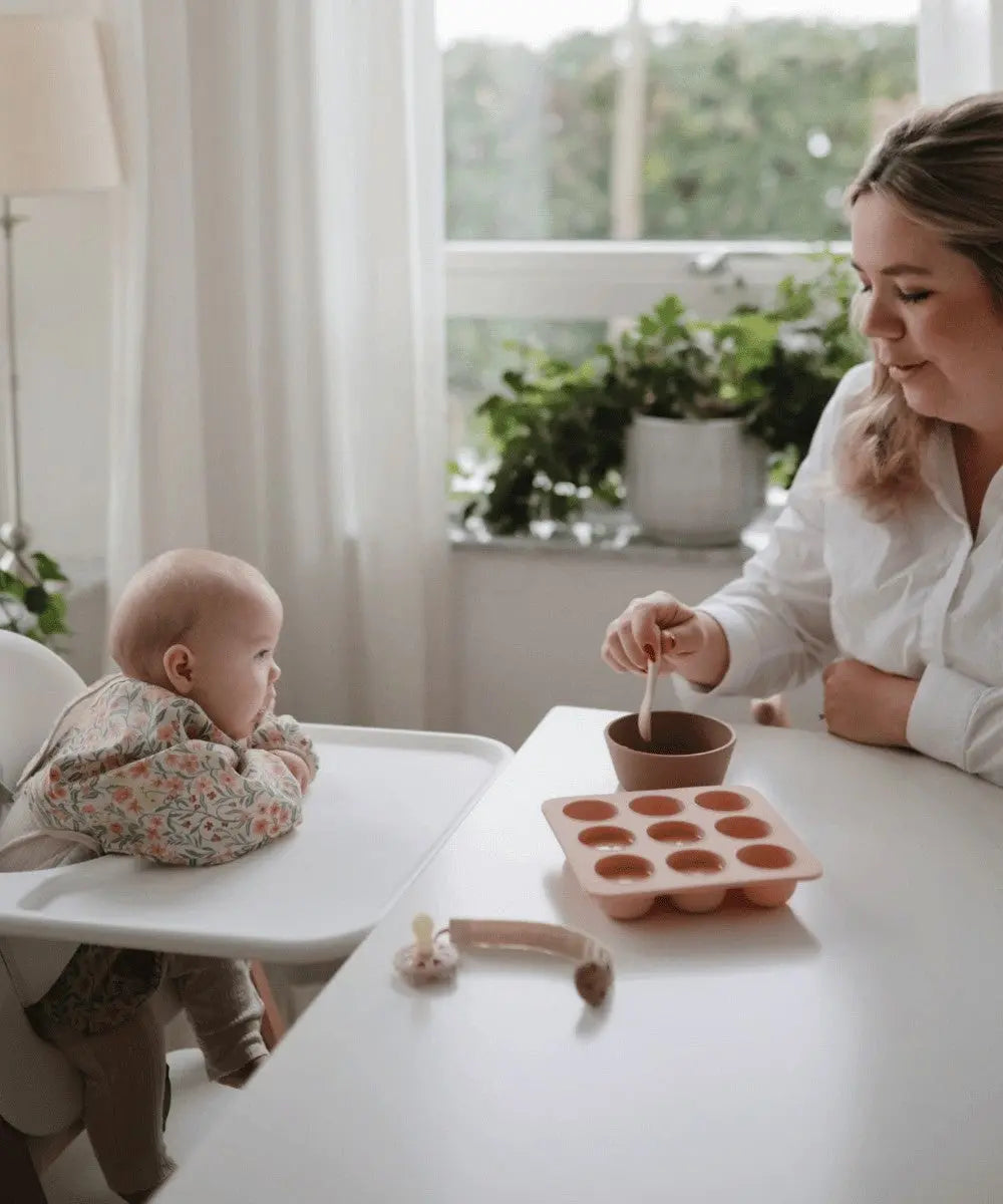 Bébé portant le Bavoir à manches longues Pastel Blooms de Mushie pendant son repas