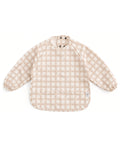 Bavoir tablier à manches longues Jolis carreaux de Mrs Ertha, à carreaux crème et beige et petits cœurs, sur fond blanc