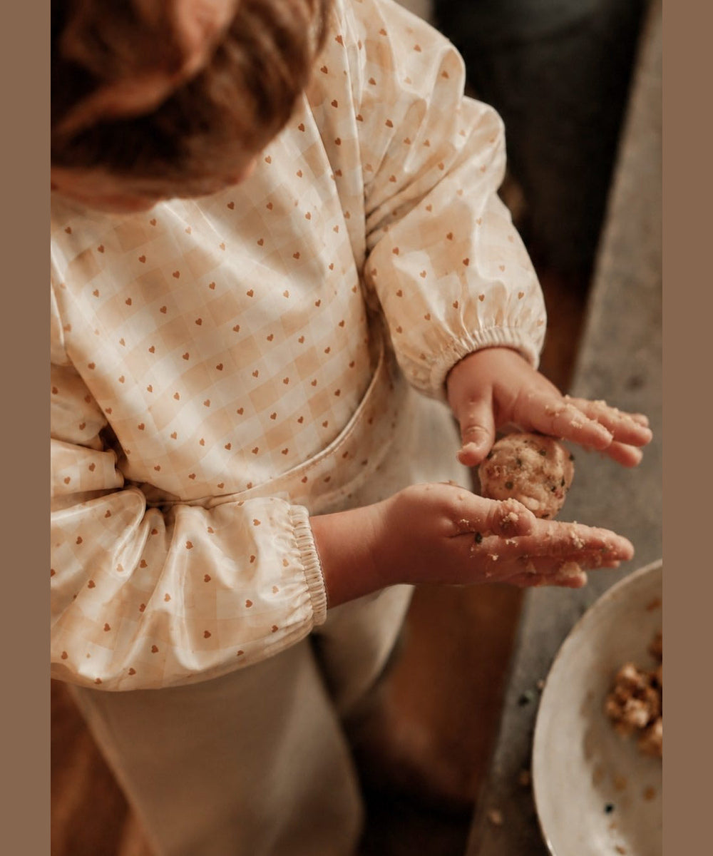 Enfant portant le bavoir à manches longues Jolis carreaux de Mrs Ertha pendant un atelier de pâtisserie