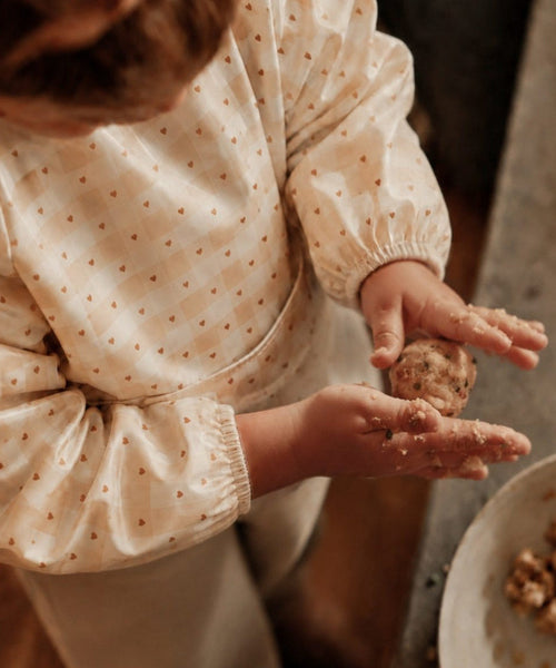 Enfant portant le bavoir à manches longues Jolis carreaux de Mrs Ertha pendant un atelier de pâtisserie