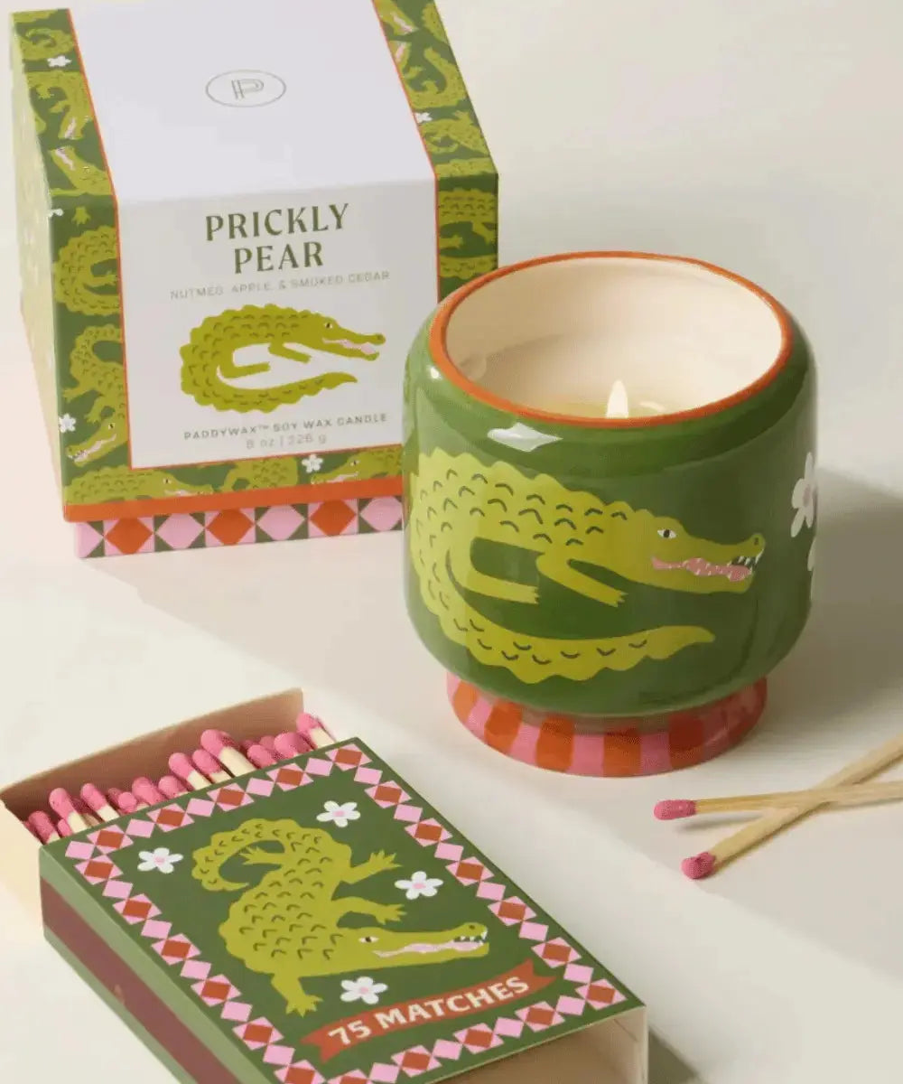 Bougie crocodile Adopo posée sur une table à côté de sa jolie boîte cadeau et d'allumettes