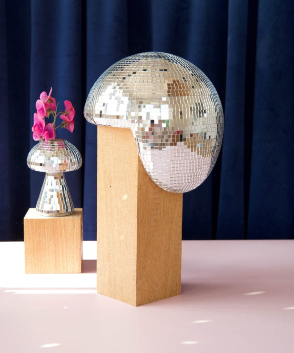 Boule disco fondue présentée sur un socle devant un rideau bleu