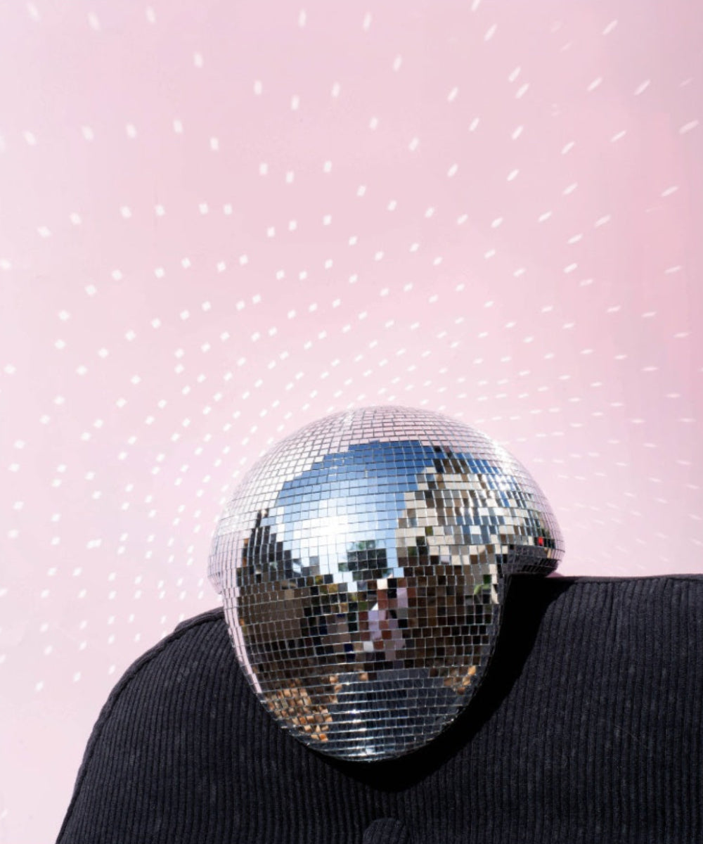 Boule disco fondue posée sur un fauteuil noir devant un mur rose