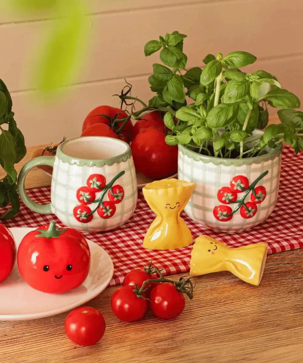 Cache-pot Tomato posé sur une table coloré et contenant un pied de basilic