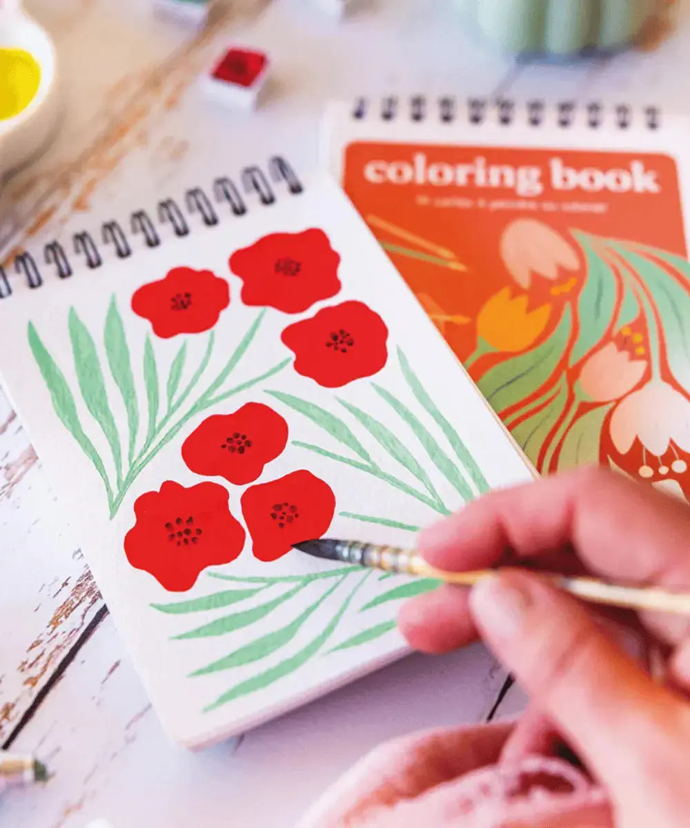 Personne en train de peindre des coquelicots sur le carnet de coloriage Fleurs de Maison Joliette