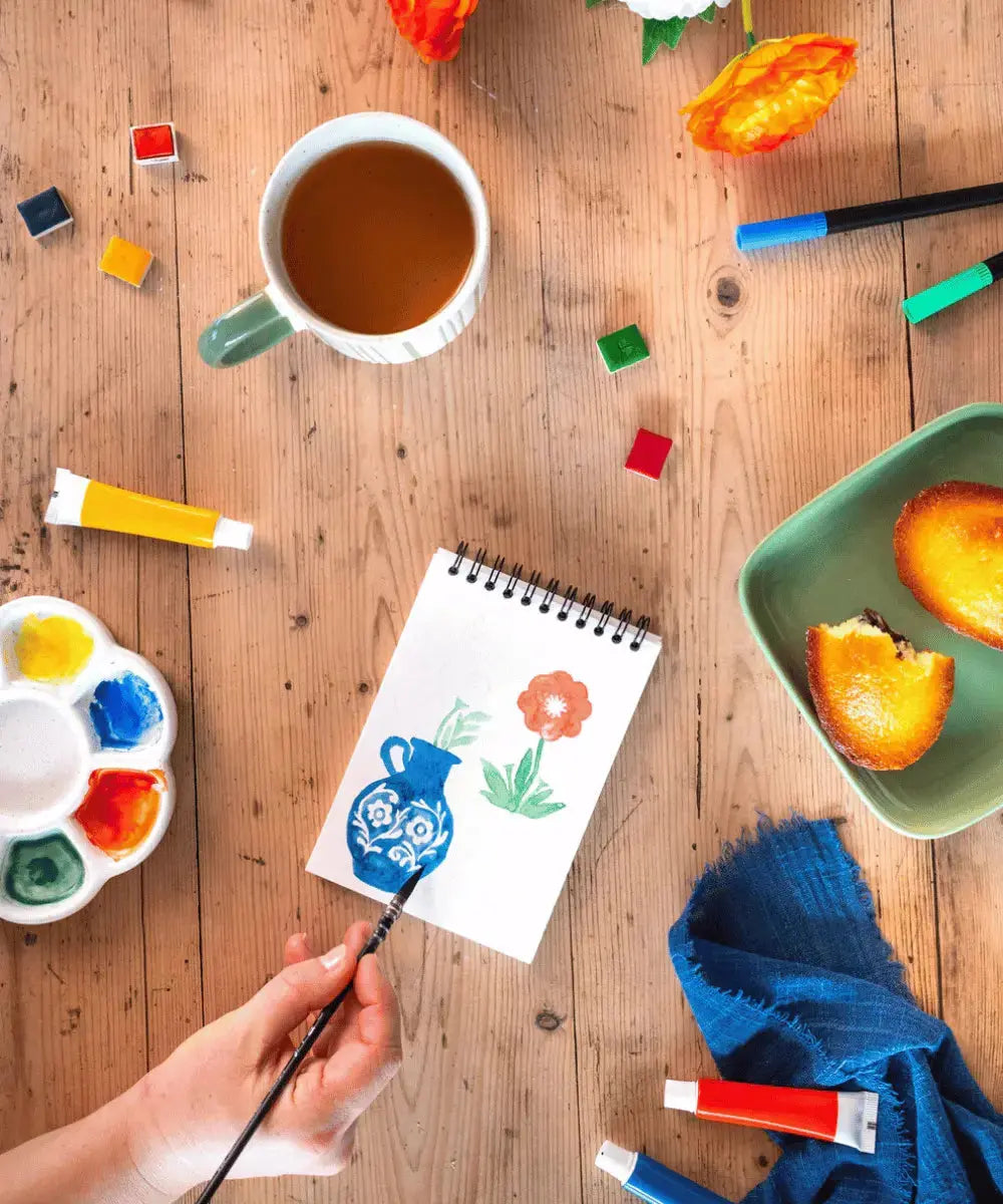 Carnet de coloriage Bloom posée sur une table accompagné de tubes de peinture