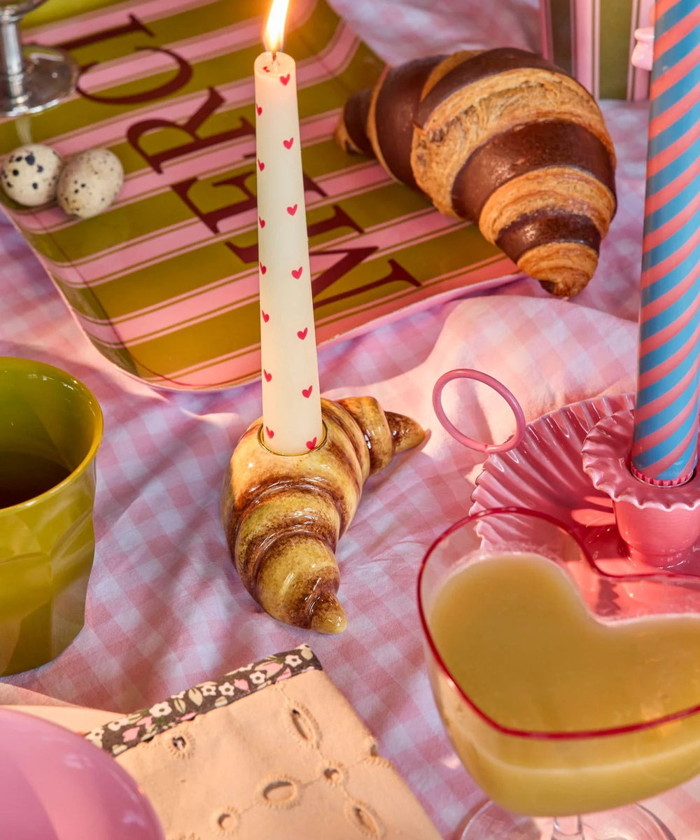 Bougeoir en céramique marron émaillée en forme de croissant au beurre posé sur une table colorée