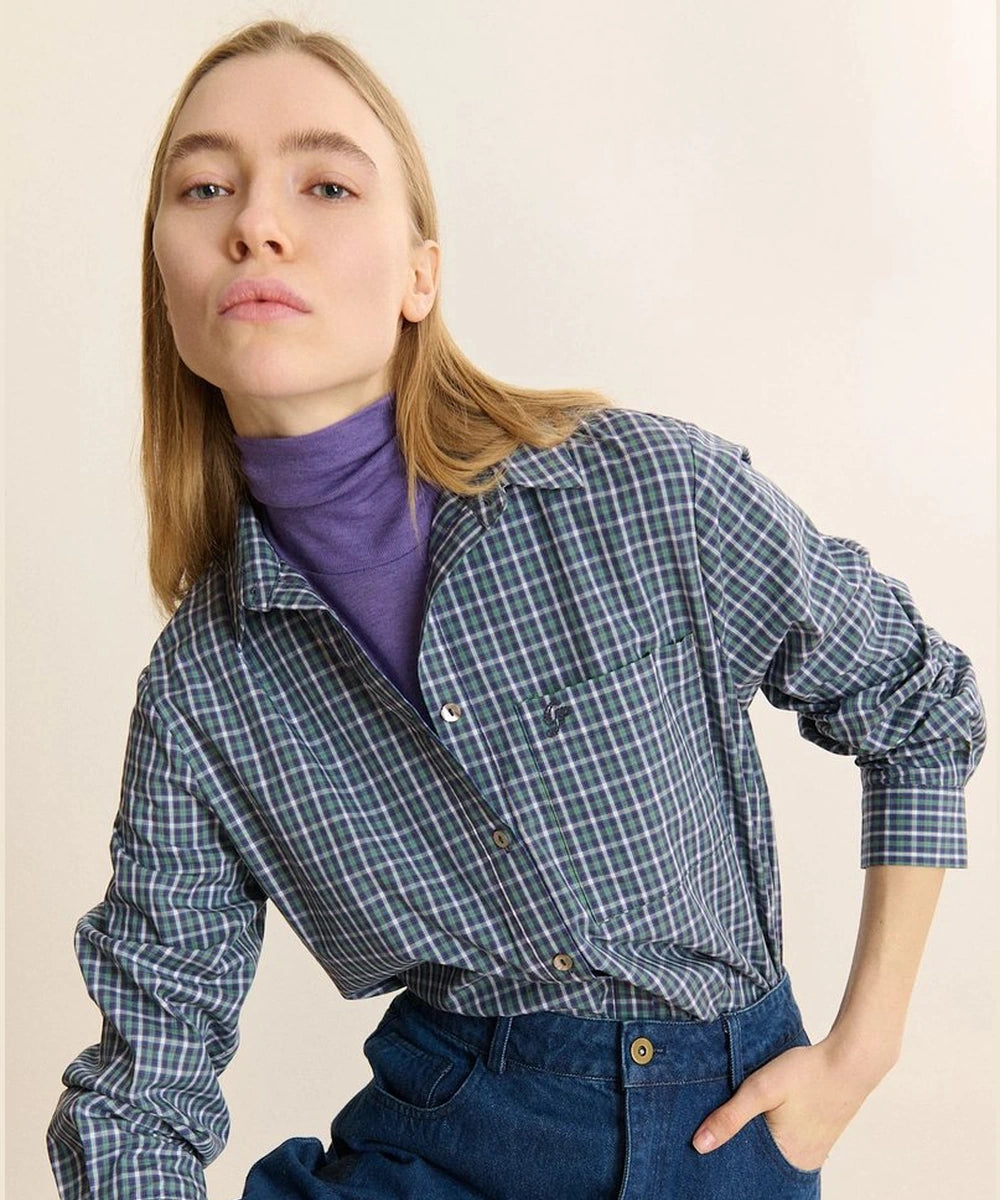 Chemise Ted verte de Garance Paris portée sur un col roulé violet, avec les mains dans les poches