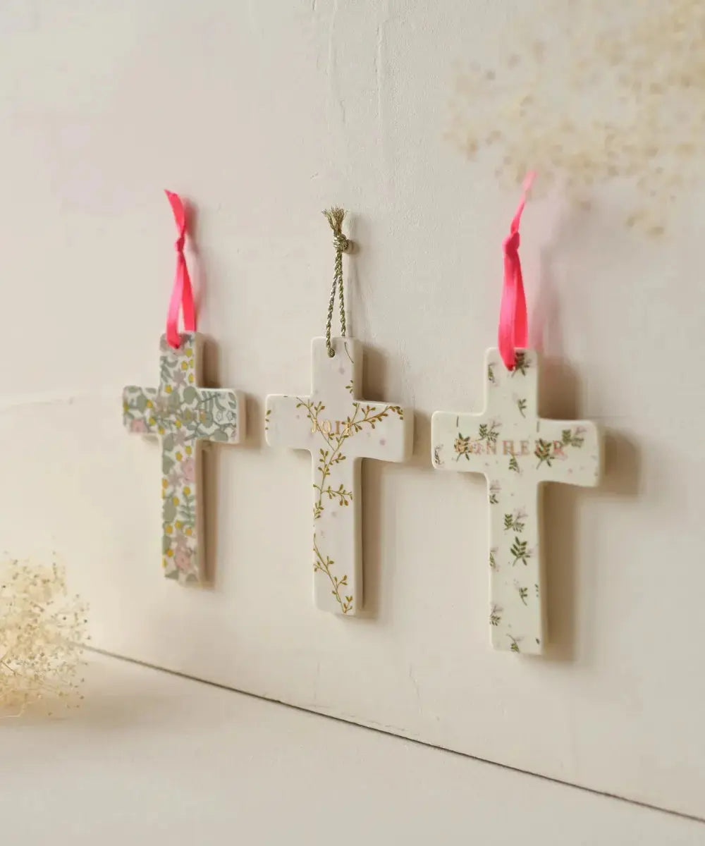 Croix en porcelaine Bonheur motif fleuri Lily de la marque Baubels et suspendue à un mur