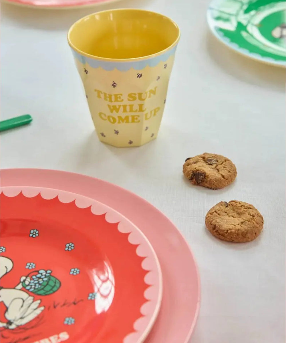 Gobelet en mélamine Snoopy rouge posé sur une table dressée avec des assiettes et des verres de la collection Snoopy