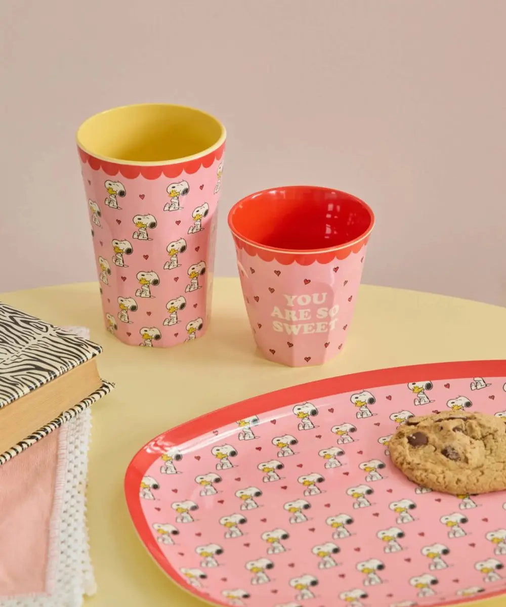 Gobelet en mélamine Snoopy rouge posé sur une table dressée avec grand gobelet et assiette de la collection Snoopy