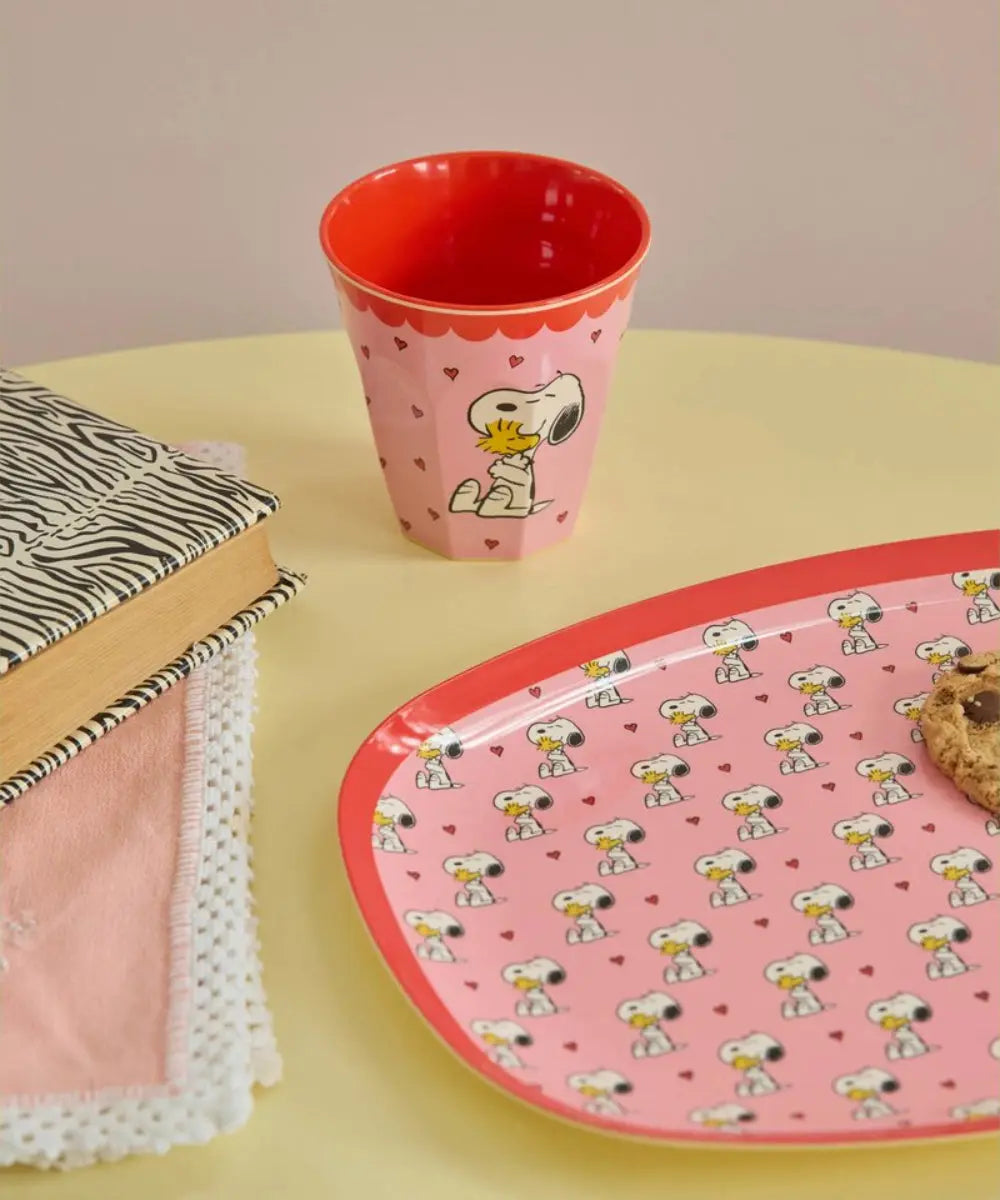 Gobelet en mélamine Snoopy rose posé sur une table avec une assiette de la collection Snoopy