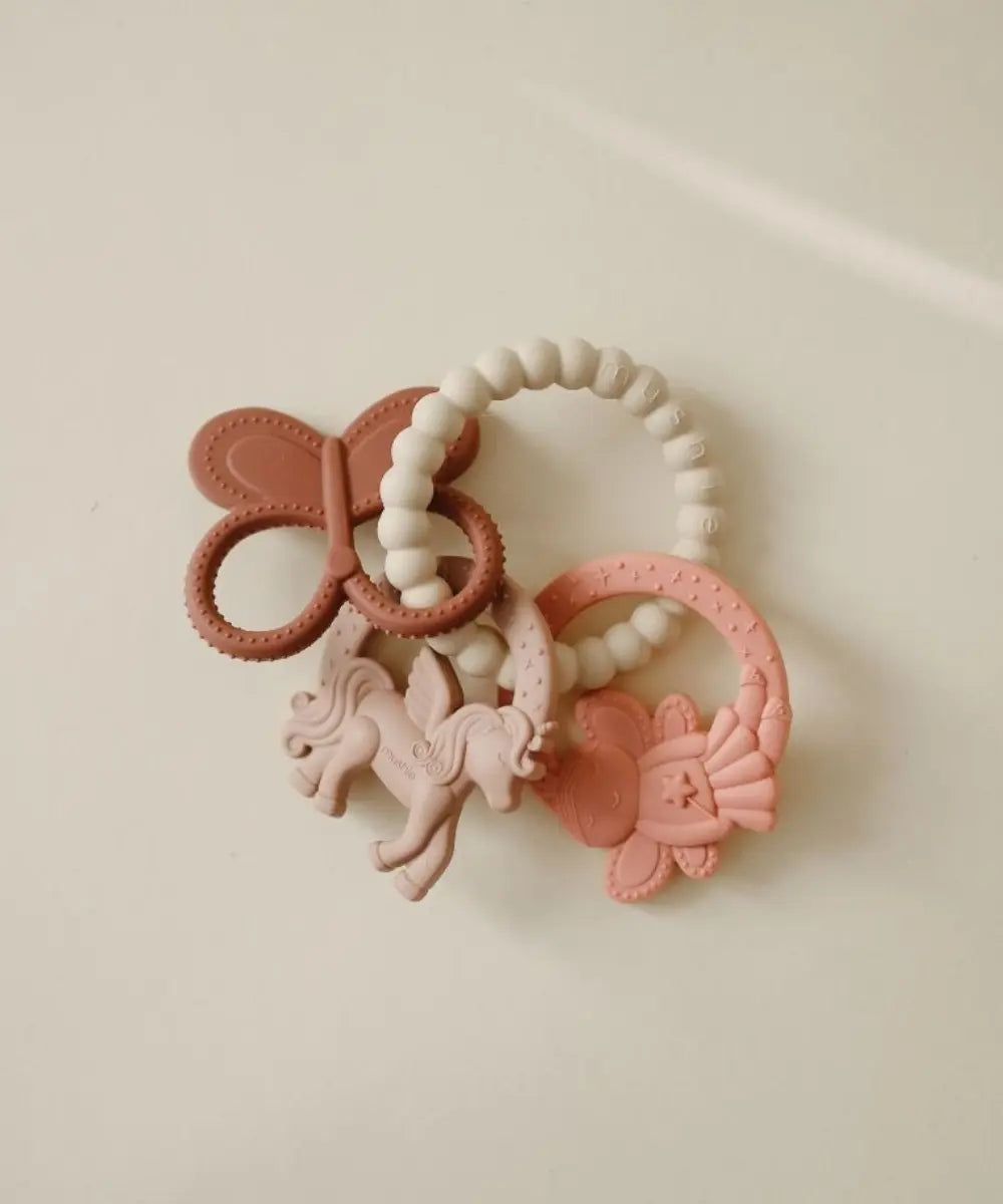 Anneau de dentition en silicone rose poudré avec formes de licorne et papillon Mushie.