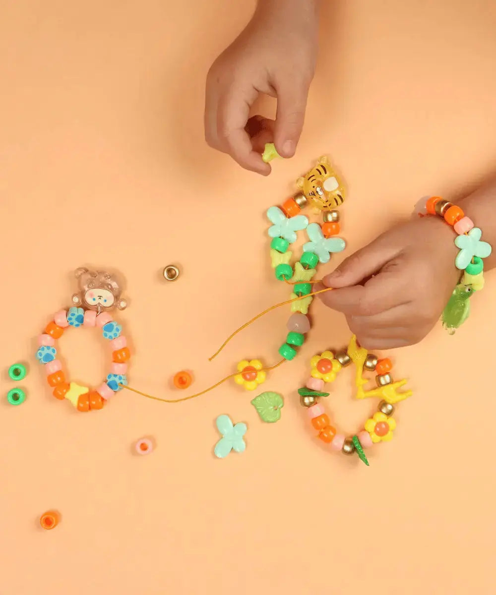 Enfant en train de fabriqué un collier avec les perles colorés du kit créatif Mes Premiers Bijoux Animaux de Auzou