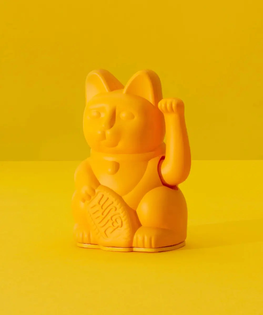 Petit chat porte-bonheur japonais Maneki Neko couleur jaune moutarde mat qui fait signe de la patte.