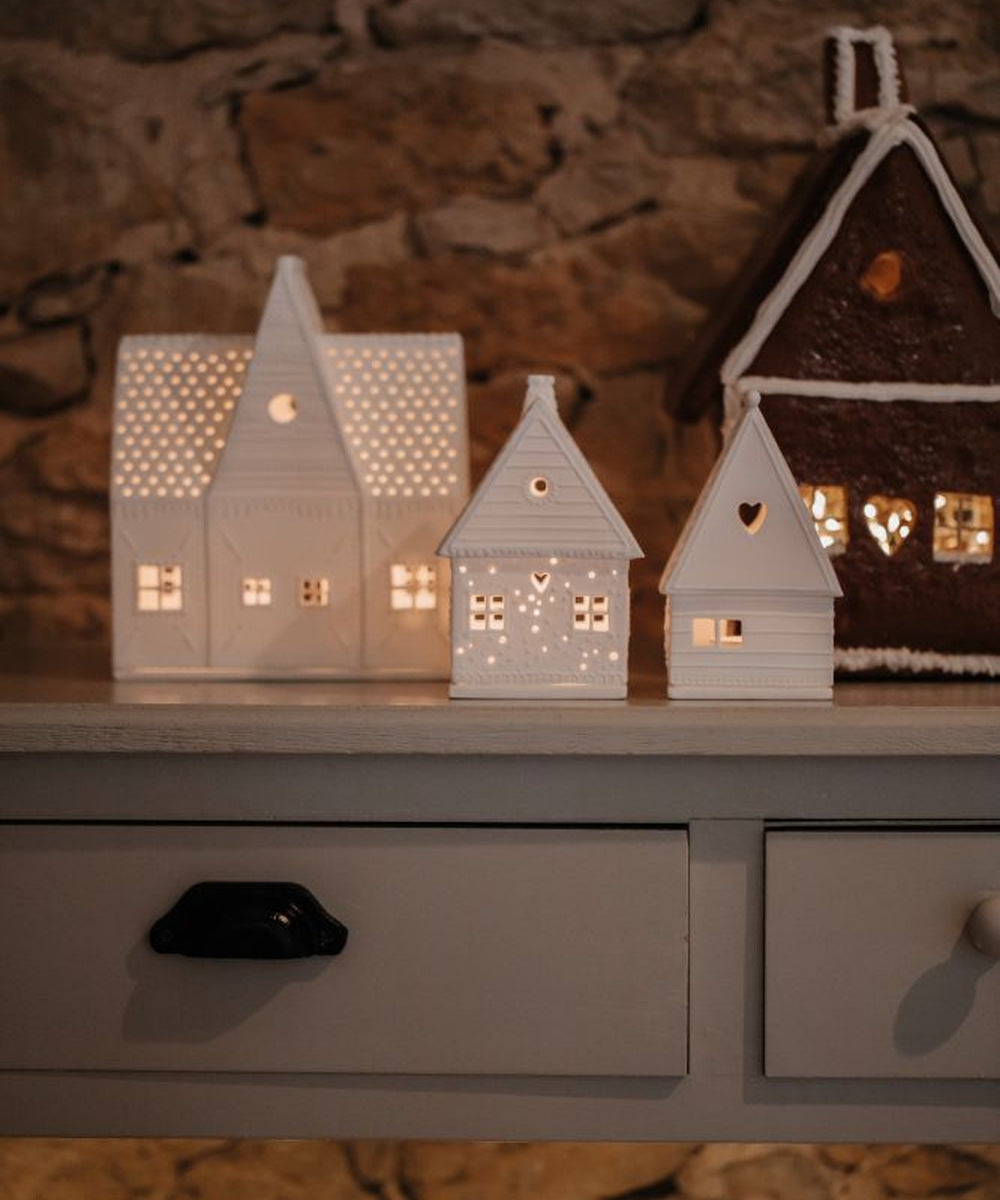Maison photophore Pain d'épices Cœur de Räder illuminée à droite d'un village de maisons en porcelaine sur une commode