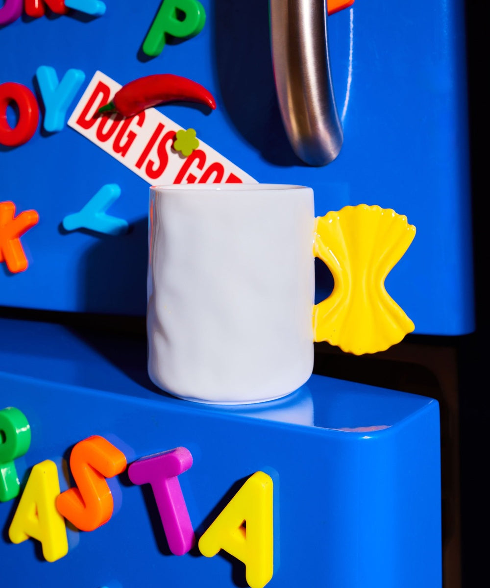 Mug Pasta blanc à anse farfalle jaune dans une mise en scène colorée sur fond bleu