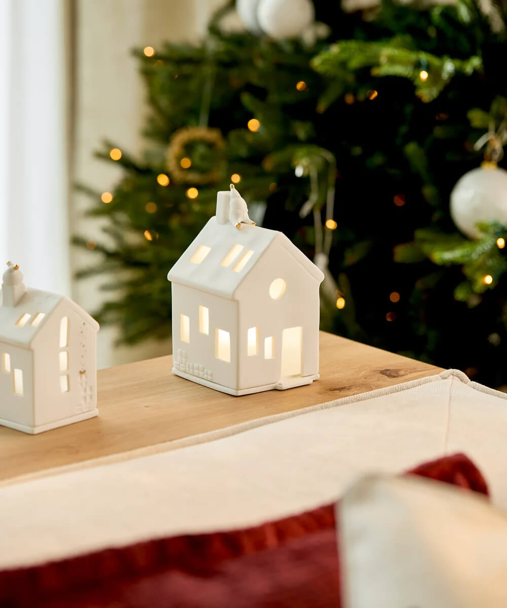 Maison photophore En attendant Rudolf de Räder illuminée sur une console devant un sapin de Noël
