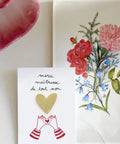 Petit pin's en laiton en forme de cœur doré brillant posé sur sa carte cadeau illustrée Merci Maîtresse.