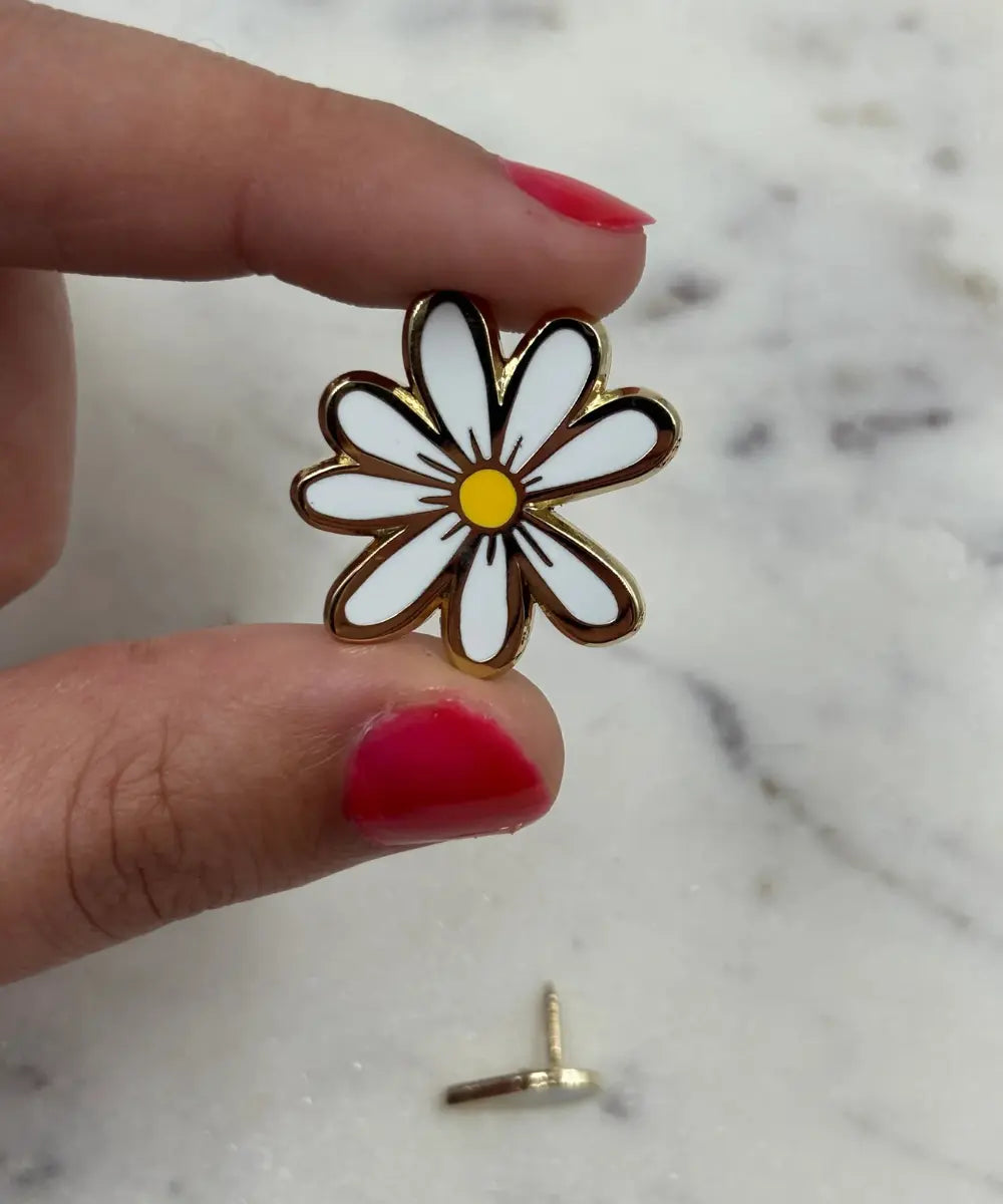 Petit pin's émaillé en forme de marguerite blanche aux contours dorés sur sa carte cadeau.