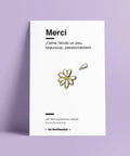 Petit pin's émaillé en forme de marguerite blanche aux contours dorés sur sa carte cadeau.
