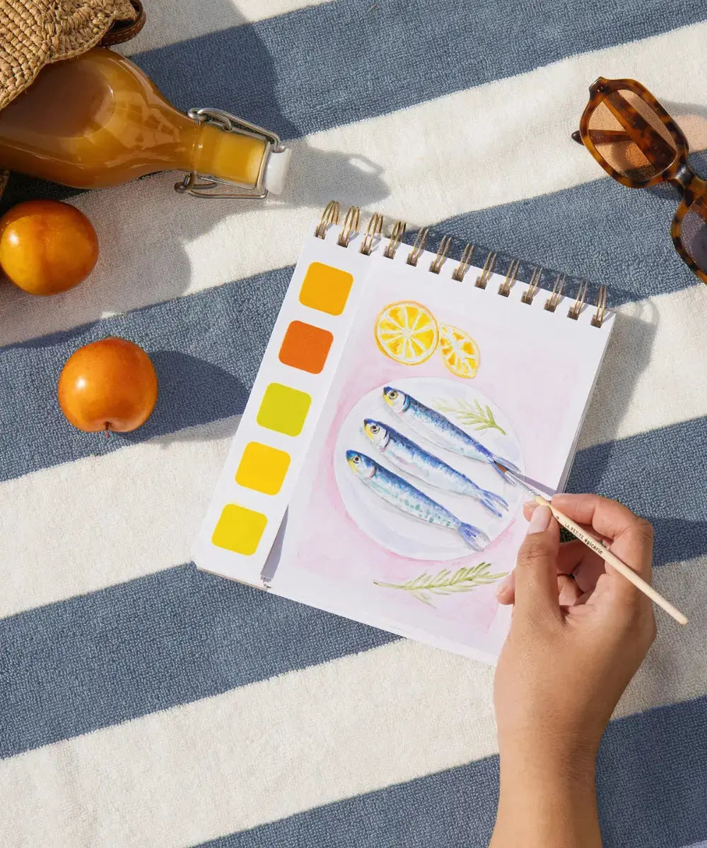 Femme en train de réaliser une illustration du Carnet d'aquarelle Travel Book Méditerranée de la marque La Petite Epicerie