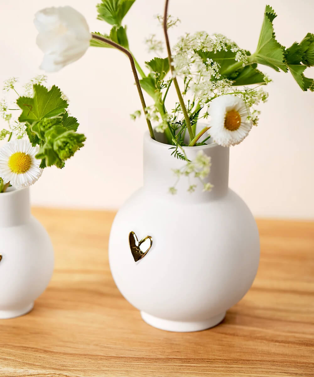 Vase boule Cœur doré de Räder avec un bouquet de fleurs blanches sur un meuble en bois