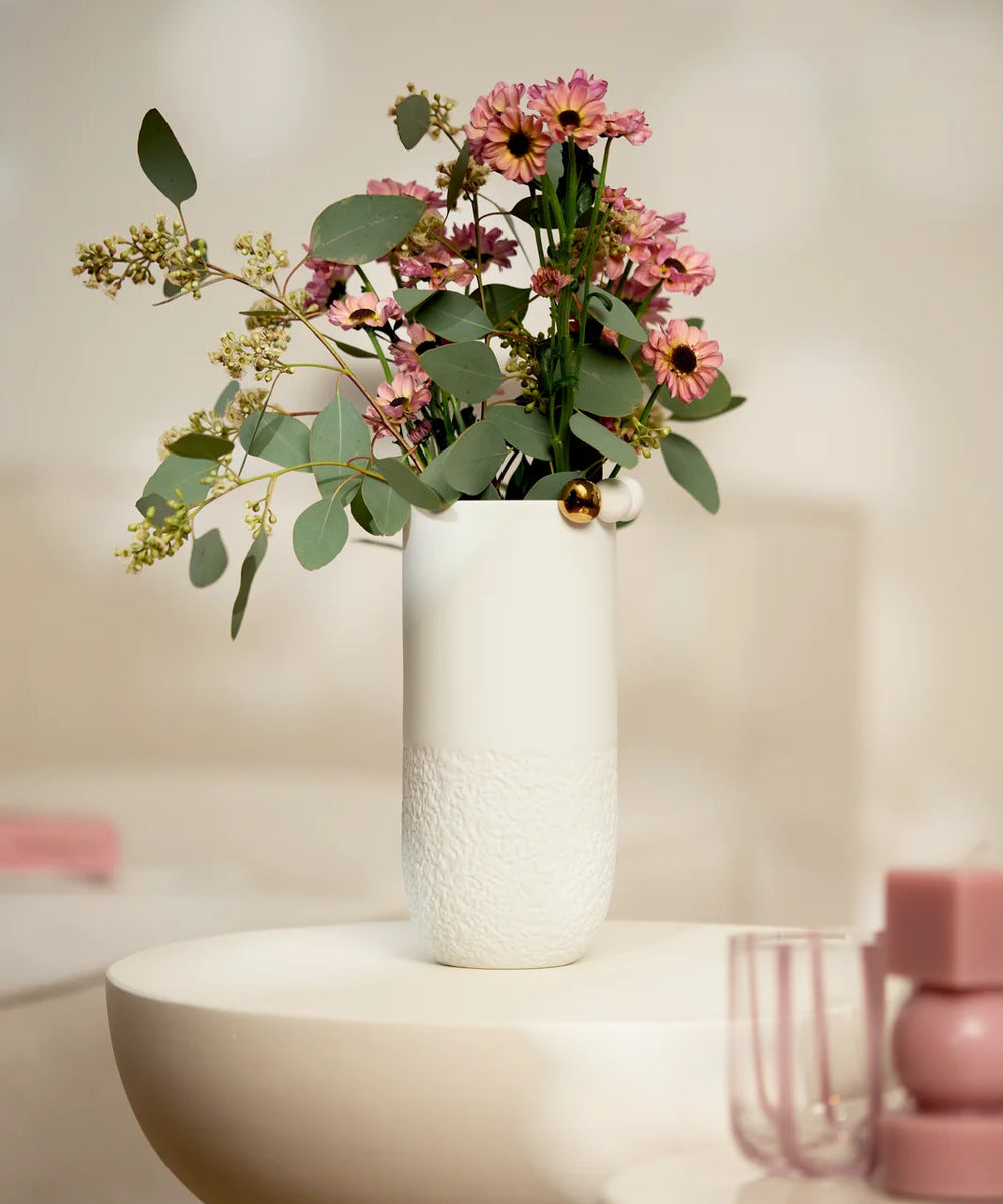 Vase Paysage enneigé de Räder garni de fleurs roses et de feuillage sur une table claire