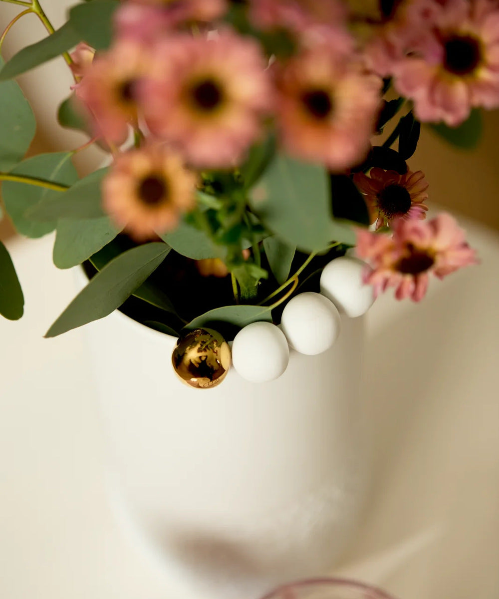 Détail des boules blanches et dorée sur le bord du vase Paysage enneigé de Räder avec un bouquet de fleurs roses