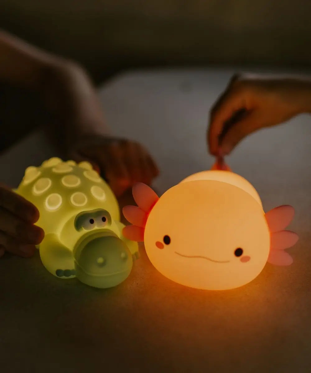 Veilleuse pour enfant en silicone souple rose en forme d'axolotl illuminée la nuit.