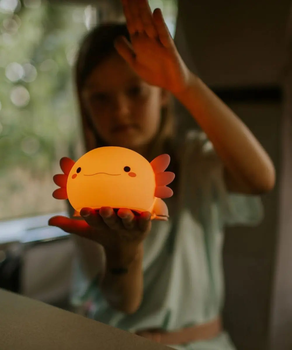 Veilleuse pour enfant en silicone souple rose en forme d'axolotl manipulée par un enfant